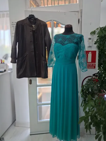 Vestido de fiesta de encaje turquesa junto a un abrigo de cuero, expuestos en la entrada del taller