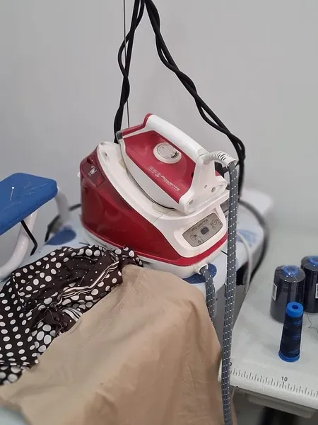 Plancha de vapor con prendas listas para planchar en el taller